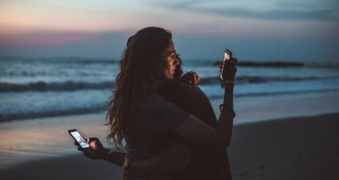 Para przytulająca się i patrząca na swoje telefony na plaży